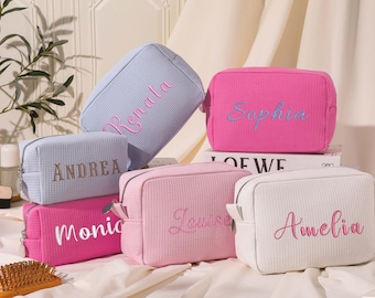 May include: Six different cosmetic bags with personalised names. The bags are made of a soft, textured fabric and come in a variety of colours, including pink, blue, and white.