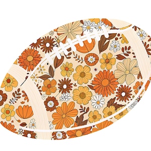 May include: An illustrated football with a floral pattern in shades of orange, yellow, and brown. The design features various flower shapes and sizes, with white stitching details. The background is a light beige color.