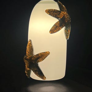 Puede incluir: Una lámpara colgante de vidrio blanco con dos detalles de libélula de color dorado.