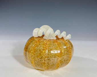 May include: A glass pumpkin with a swirl design on top. The pumpkin is a light brown color with a speckled texture.