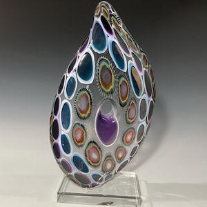 May include: A clear glass sculpture with a purple, white, and blue abstract design. The sculpture is on a clear glass base.