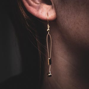 May include: Gold dangle earrings with a chain and a small round charm at the bottom.