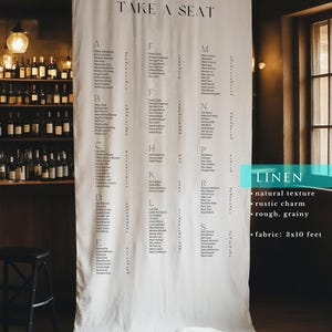 May include: A large, off-white linen fabric seating chart hanging vertically, featuring the text "TAKE A SEAT" at the top followed by an alphabetical list of names and table numbers. The fabric measures 0.91 by 3.05 metres and has a visible texture.