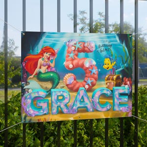 May include: A colorful birthday banner with a mermaid, a large number 5, and the name "GRACE" in glittery letters. The banner has a blue, green, and pink color scheme and features seashells, starfish, and a treasure chest.