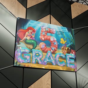 May include: A colorful birthday banner featuring a mermaid with a crown, a large number 5, and the name "GRACE" in sparkly letters. The banner has a blue and green ocean background with seashells and starfish.