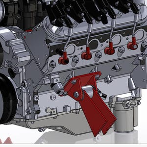 May include: A computer-aided design rendering of a V8 engine block featuring a prominent red metal mounting bracket attached to the side. The engine assembly includes black pulleys, silver metallic components, and red spark plug wire boots.
