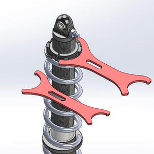 May include: A detailed view of a shock absorber with a silver spring and black components. Two red spanner wrenches are positioned on the shock absorber, suggesting adjustment or maintenance. The image is a technical illustration.