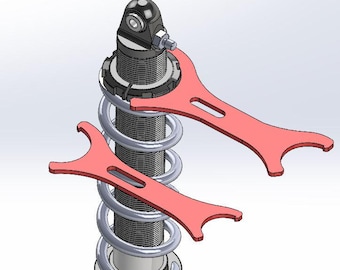 May include: A detailed view of a shock absorber with a silver spring and black components. Two red spanner wrenches are positioned on the shock absorber, suggesting adjustment or maintenance. The image is a technical illustration.