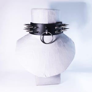 Könnte beinhalten: Ein schwarzes Lederhalsband mit silbernen Spikes und einem silbernen Ring.