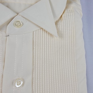 May include: Cream-colored dress shirt with a pleated front and a classic collar. The shirt has a button-down closure and the label reads "L&M Fashions PERMANENT PRESS MS 65% POLYESTER 35% COTTON". The phone model "Galaxy S21 Ultra 5G" is visible.