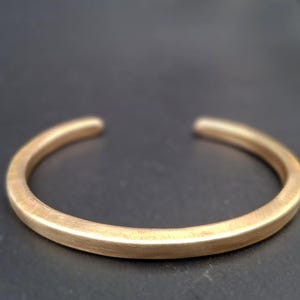 Peut inclure: Un bracelet manchette de couleur or avec un design simple et ouvert. Le bracelet a une finition lisse et mate et une forme arrondie. Les extrémités ouvertes permettent de le porter facilement. Ce bijou minimaliste convient au quotidien.