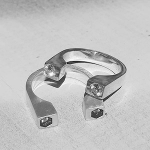 Puede incluir: Dos anillos de plata con un diseño hexagonal y una pequeña piedra preciosa transparente engastada en cada anillo.