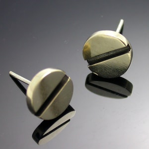 May include: A pair of gold-toned stud earrings with a simple, minimalist design. Each earring features a round disc with a single, horizontal line across the center.
