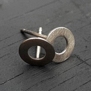 Pode incluir: Um par de brincos de prata com um design simples e moderno. Cada brinco apresenta dois círculos sobrepostos, criando um visual único e minimalista.