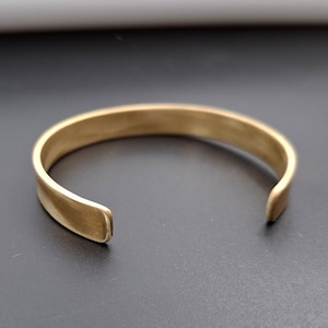 Peut inclure: Un bracelet jonc simple en métal doré. Le bracelet est ouvert et a une finition lisse et arrondie.