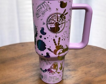 May include: A pink stainless steel travel mug with a handle. The mug has a variety of graphics on it, including a compass, a jeep, and ducks. The mug has a white lid.