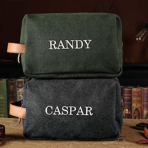 May include: Two green and black canvas travel bags with leather handles. The top bag has the name "RANDY" embroidered on it. The bottom bag has the name "CASPAR" embroidered on it.
