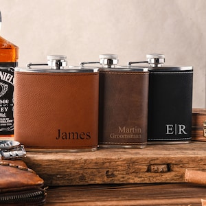 Pode incluir: Três cantis de aço inoxidável revestidos com material semelhante a couro nas cores castanho, castanho escuro e preto. Cada cantil possui uma tampa de rosca e uma gravação personalizada: James no castanho, Martin Groomsman no escuro e E|R no preto.