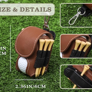 K&ouml;nnte beinhalten: Braune Golfballhalterung aus Leder mit einem wei&szlig;en Golfball, Holz-Tees und einem Metallclip. Der Halter ist 10 cm hoch und 6 cm breit. Der Halter hat wei&szlig;e N&auml;hte und schwarze Gummib&auml;nder f&uuml;r die Tees.