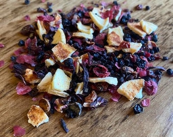 May include: A loose leaf fruit tea blend consisting of dried dark purple berries, vibrant red hibiscus petals, and light beige pieces of dried citrus peel scattered in a small pile, showcasing a mix of textures and natural colors.