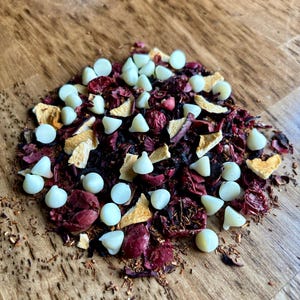 May include: A close-up of a loose leaf tea blend with white chocolate chips, dried fruit pieces, and red flower petals.
