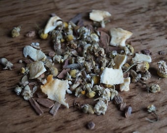 May include: A close-up of a mix of dried herbs and flowers, including chamomile, lemon peel, and cinnamon sticks. The mixture is a light brown color and has a variety of textures.
