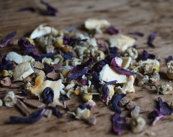 May include: A mix of dried herbs and flowers for tea, including purple hibiscus, white chamomile, and orange peel.