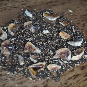 May include: A close-up of a mixture of dried black tea leaves and small pieces of dried fruit. The fruit pieces are light brown and have a slightly translucent appearance.