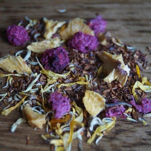 May include: A blend of loose leaf tea with dried pineapple, dried fruit, and flower petals. The tea is a mix of brown, yellow, and purple.