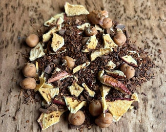 May include: A close-up of a pile of loose-leaf tea blend. The blend includes small, round, tan-colored pieces, along with dried fruit pieces and dark brown tea leaves. The tea is on a wooden surface.