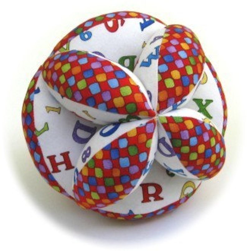 Puede incluir: Una pelota de tela multicolor con fondo blanco y cuadrados rojos, azules y amarillos. La pelota est&aacute; hecha de varios paneles de tela y tiene las letras del alfabeto impresas.