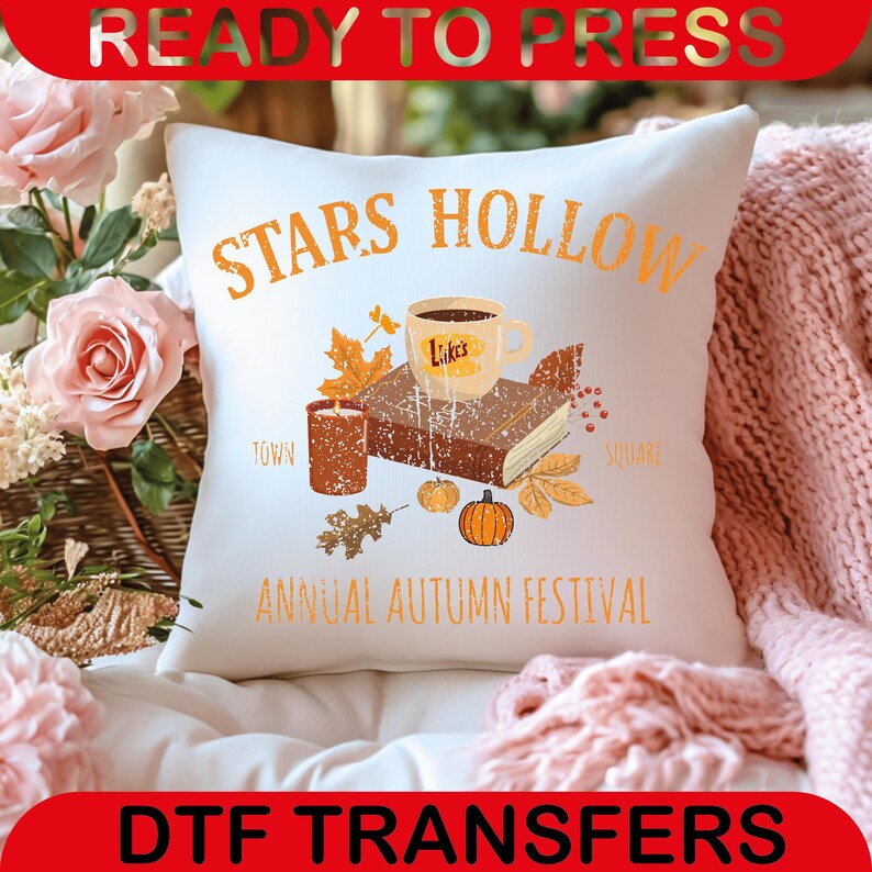 May include: White decorative pillow with an autumn-themed design. The pillow features the text "STARS HOLLOW" and "ANNUAL AUTUMN FESTIVAL". The design includes a coffee cup, book, candle, pumpkins, and fall leaves.