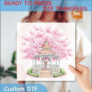 May include: A watercolor illustration of a gazebo surrounded by a blooming cherry blossom tree. The gazebo has a brown roof and white railings. The image has the text "READY TO PRESS DTF TRANSFERS" and "Custom DTF".