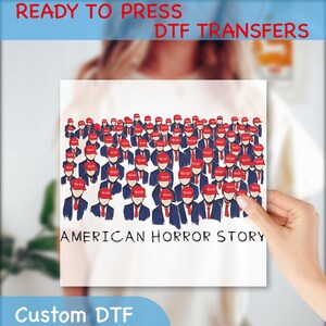 May include: DTF transfer featuring a crowd of figures in red hats, blue suits, and red ties. The words "AMERICAN HORROR STORY" are below the illustration. The text "READY TO PRESS DTF TRANSFERS" and "Custom DTF" are also present.