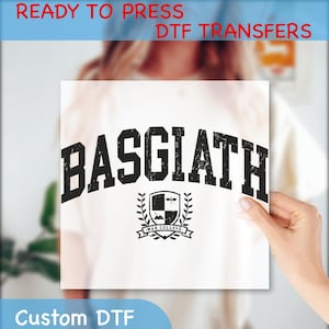 May include: A white t-shirt with a black iron-on transfer design that says "BASGIATH" in a collegiate font with a shield and laurel wreath underneath that says "WAR COLLEGE".