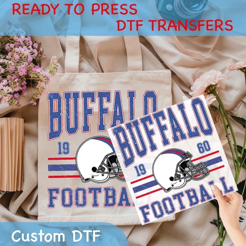 May include: A beige tote bag and a white transfer sheet featuring a distressed design with the text "BUFFALO FOOTBALL" in blue and white, along with a football helmet graphic. The text "READY TO PRESS DTF TRANSFERS" is at the top.