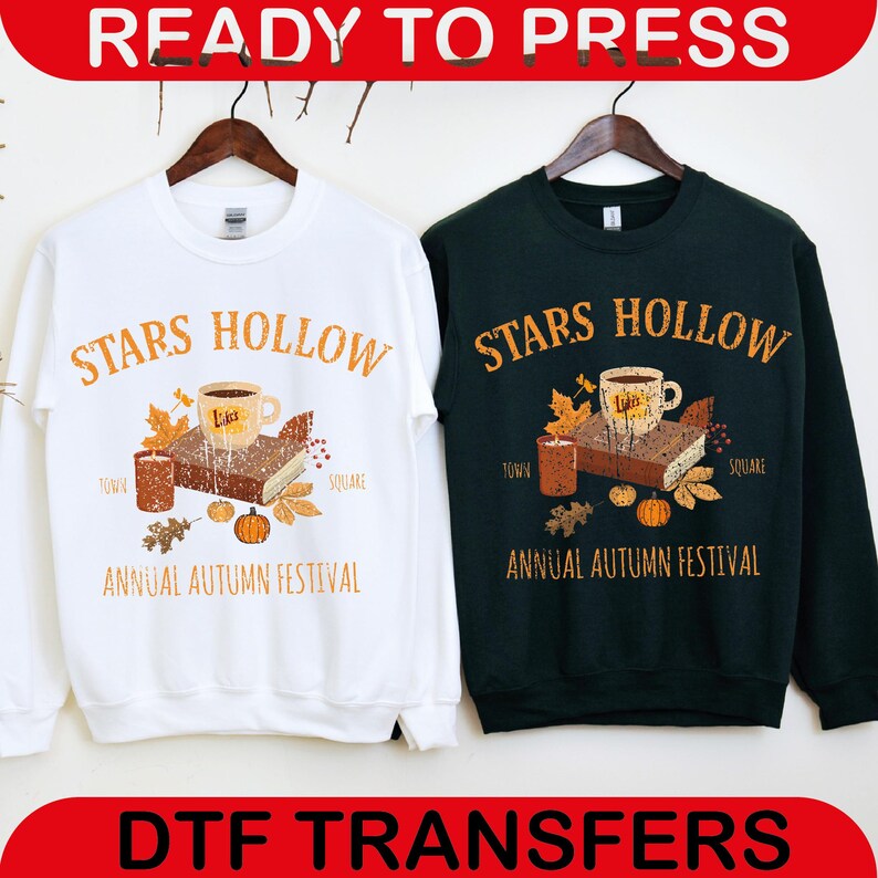 May include: White and dark green sweatshirts with the text "STARS HOLLOW" in orange. Each sweatshirt features a graphic of a coffee cup, book, candles, and pumpkins. The text "ANNUAL AUTUMN FESTIVAL" is below the graphic. The words "READY TO PRESS" and "DTF TRANSFERS" are at the top and bottom.