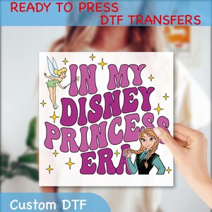 May include: A square DTF transfer with the text "IN MY DISNEY PRINCESS ERA" in purple, with Tinkerbell and Anna illustrations. The words "READY TO PRESS DTF TRANSFERS" and "Custom DTF" are also present.