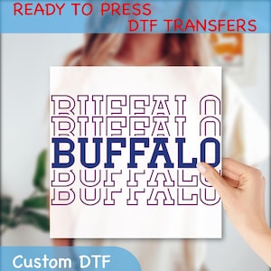 May include: A white DTF transfer sheet with the word "BUFFALO" in navy blue, repeated vertically. The words "READY TO PRESS DTF TRANSFERS" and "Custom DTF" are also visible.