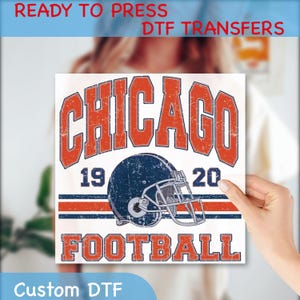 May include: A white DTF transfer featuring a distressed design with the text "CHICAGO FOOTBALL" in orange. A blue football helmet is centered below the word "CHICAGO". The years "19" and "20" are on either side of the helmet. The words "READY TO PRESS DTF TRANSFERS" and "Custom DTF" are also visible.