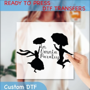 May include: A white transfer sheet with a black silhouette of two people holding umbrellas. The text "In Omnia Paratus" is written in cursive below the figures.
