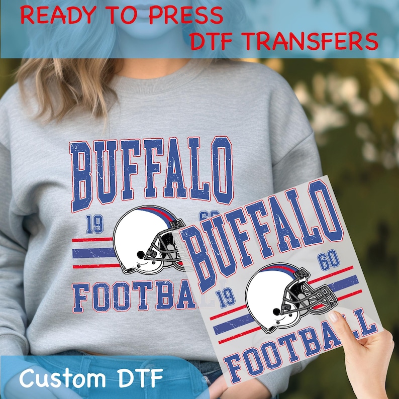 May include: Gray sweatshirt and DTF transfer featuring "BUFFALO FOOTBALL" in blue and red, with a football helmet graphic. The transfer is held up to the sweatshirt, showing the design. Text on the image reads "READY TO PRESS DTF TRANSFERS" and "Custom DTF".