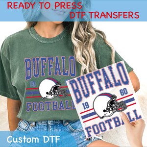 May include: A green t-shirt with the word "BUFFALO" in blue, a football helmet graphic, and the words "FOOTBALL 19" in blue and red. The image also shows a DTF transfer with the same design. Text on the image says "READY TO PRESS DTF TRANSFERS" and "Custom DTF".