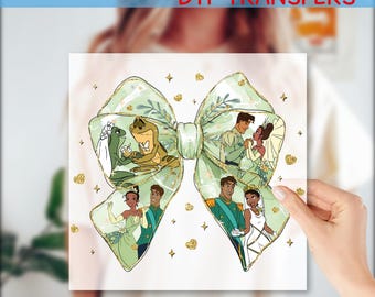 May include: A green and gold bow with a glitter finish. The bow has images of a frog prince and princess, and a human prince and princess. The image is on a clear background.