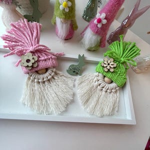 May include: Handmade gnome decorations in pink, green, and white. The gnomes feature yarn beards, wooden noses, and flower accents. Decorative bunnies are also visible. Ideal for Easter or spring home decor.