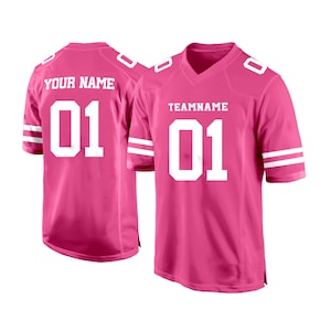 May include: Two pink football jerseys with white numbers and stripes. The jersey on the left says "YOUR NAME" and "01". The jersey on the right says "TEAMNAME" and "01".