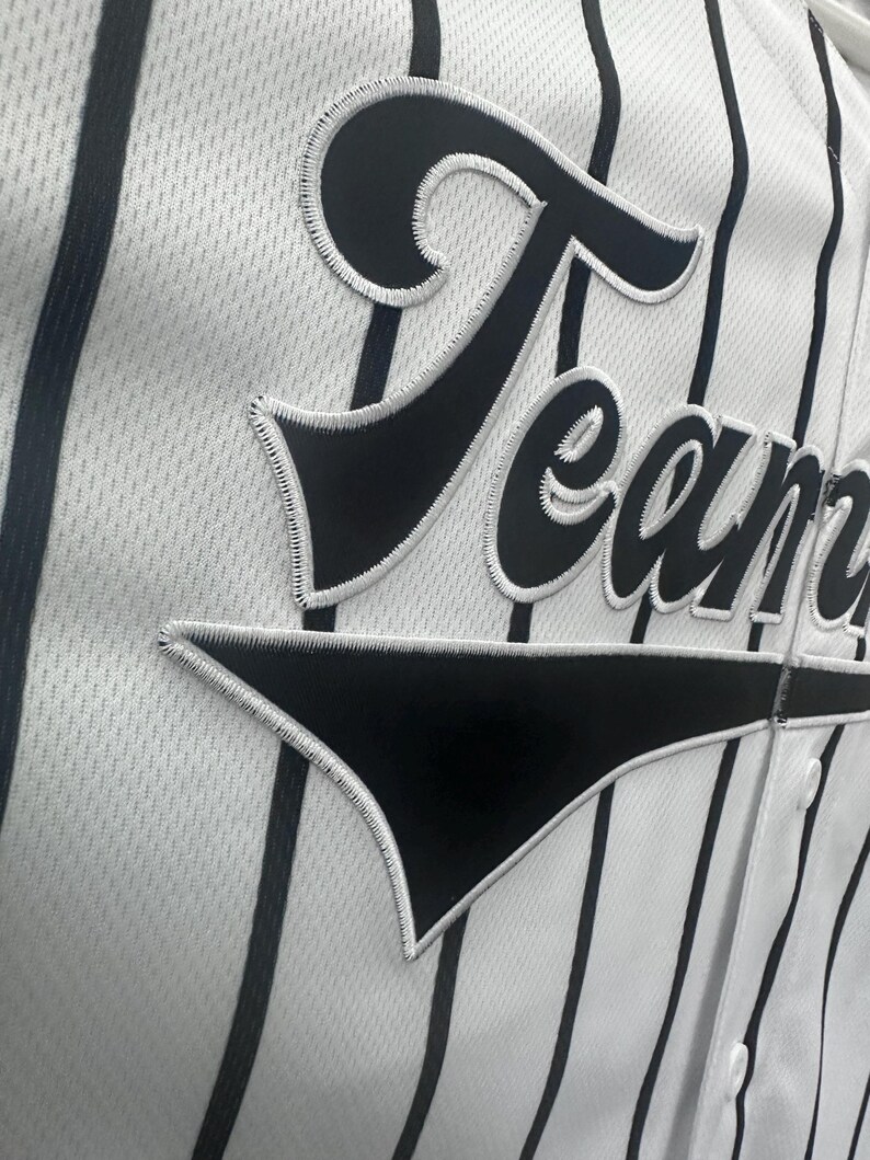 May include: White baseball jersey with black vertical stripes and a black "Team" patch on the front.