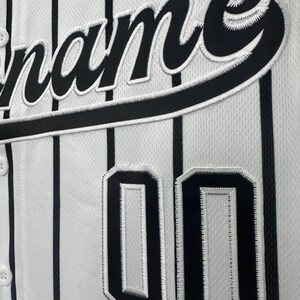 May include: White baseball jersey with black pinstripes and black embroidered lettering that says "name" and the number "00" on the front.