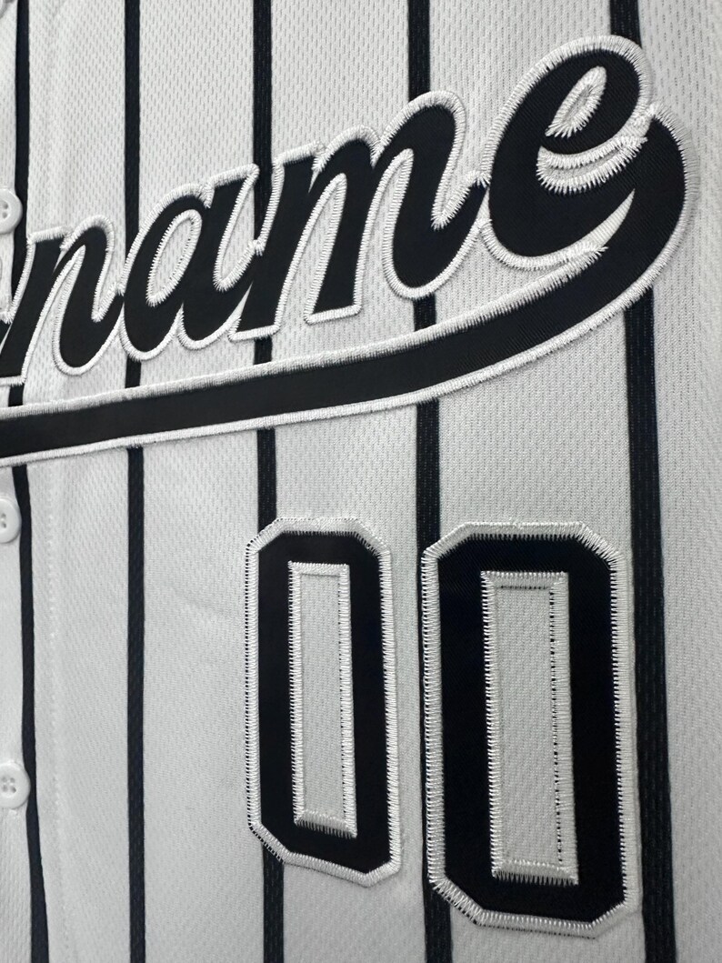 May include: White baseball jersey with black pinstripes and black embroidered lettering that says "name" and the number "00" on the front.