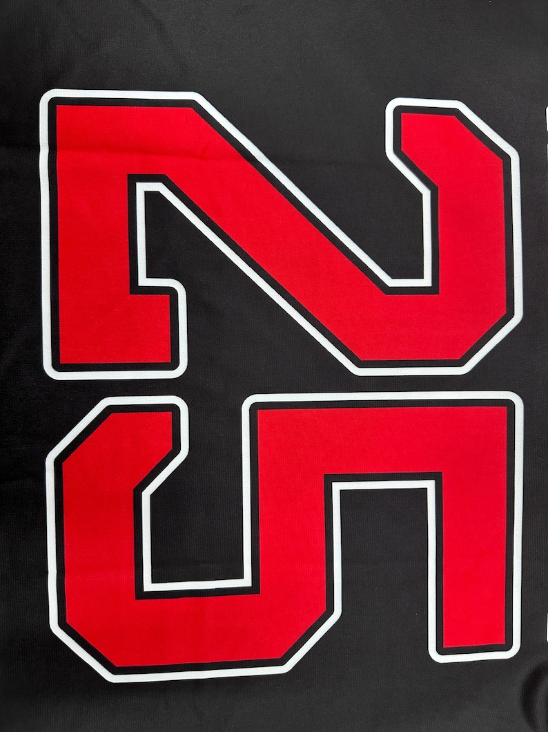 May include: Close-up of a black fabric with the number "25" prominently displayed. The numbers are red with a white border and a black outline, creating a bold, eye-catching design. The image is a close-up, focusing on the details of the numbers.